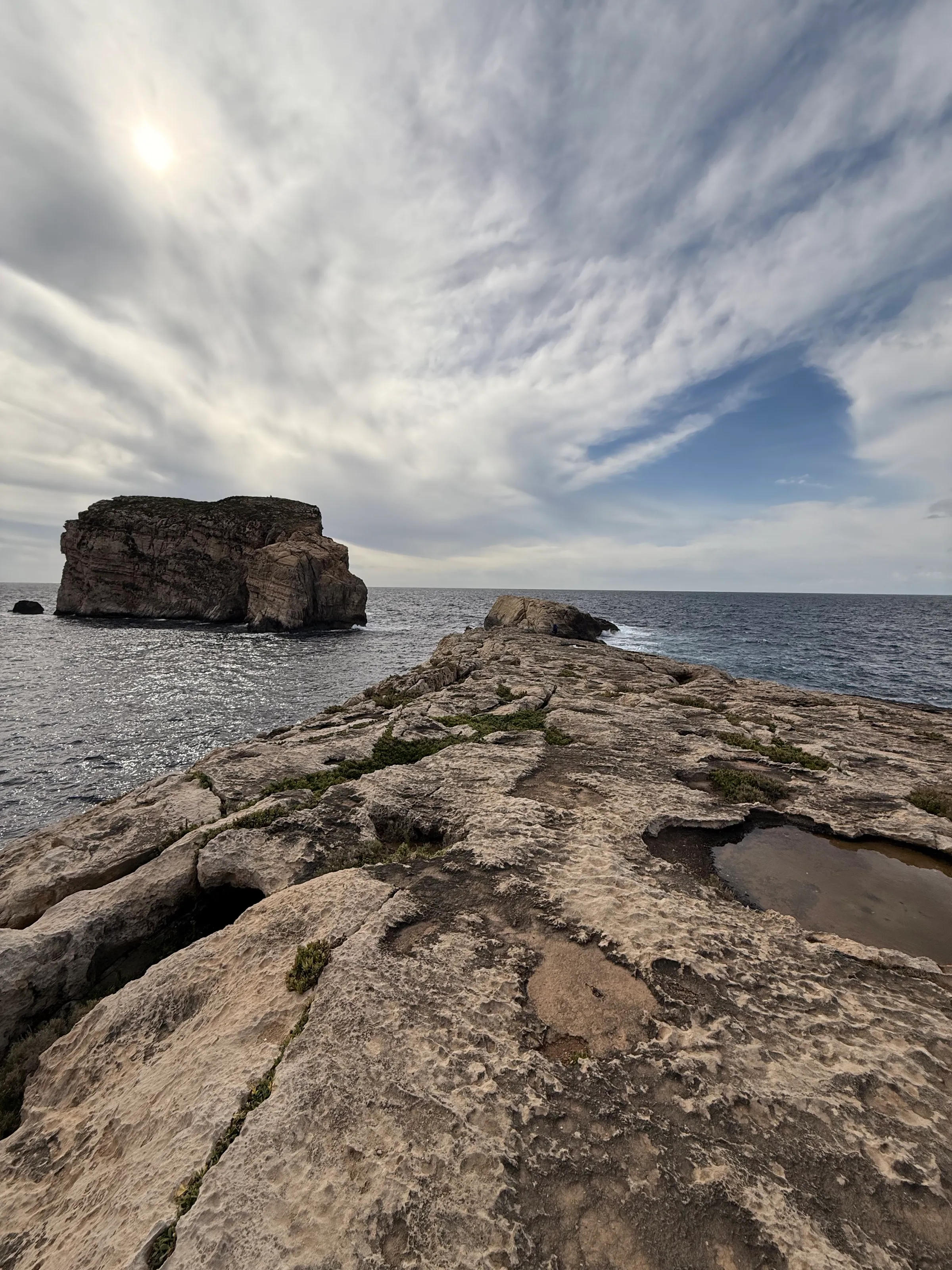 Kalksteinplatte bei Dwejra auf Gozo, dahinter ein Felsen im Meer unter bewölktem Himmel